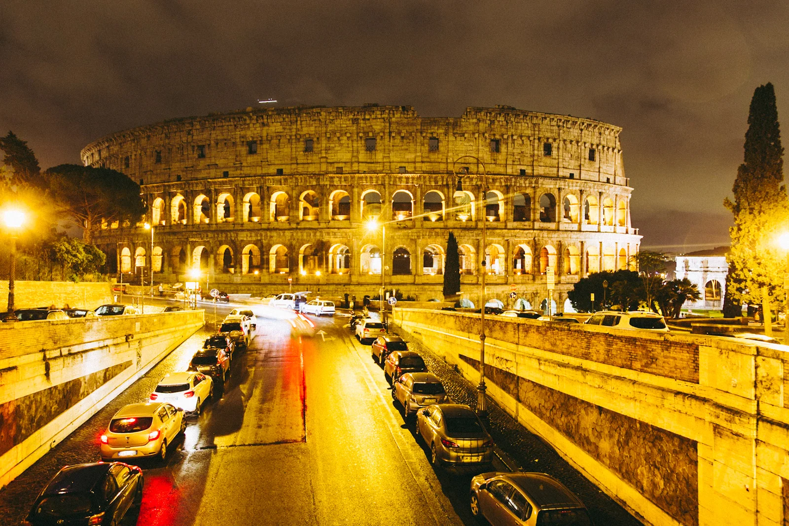 The Colosseum illuminated at night, with traffic on the road below.