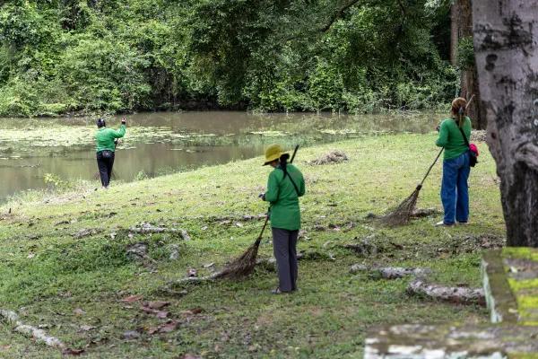 Grounds workers sweeping the grass beside the water.