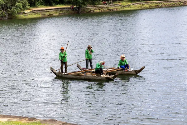 Workers in green shirts crossing the water in a wooden boat.