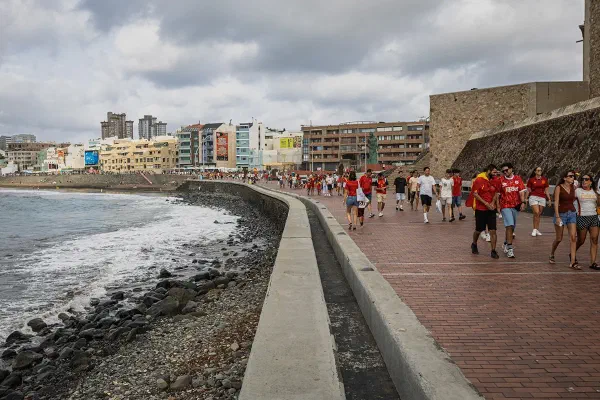 People walking along a coastal promenade in Las Palmas beneath a cloudy sky.