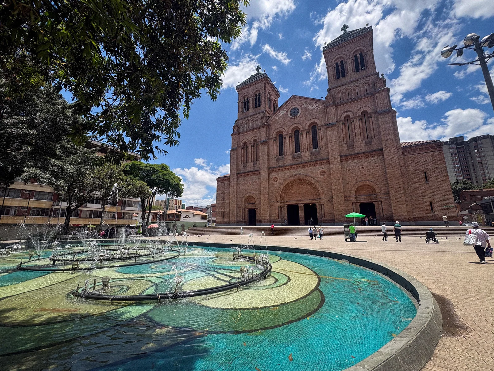 A brick church beyond a fountain in a tree-lined square.