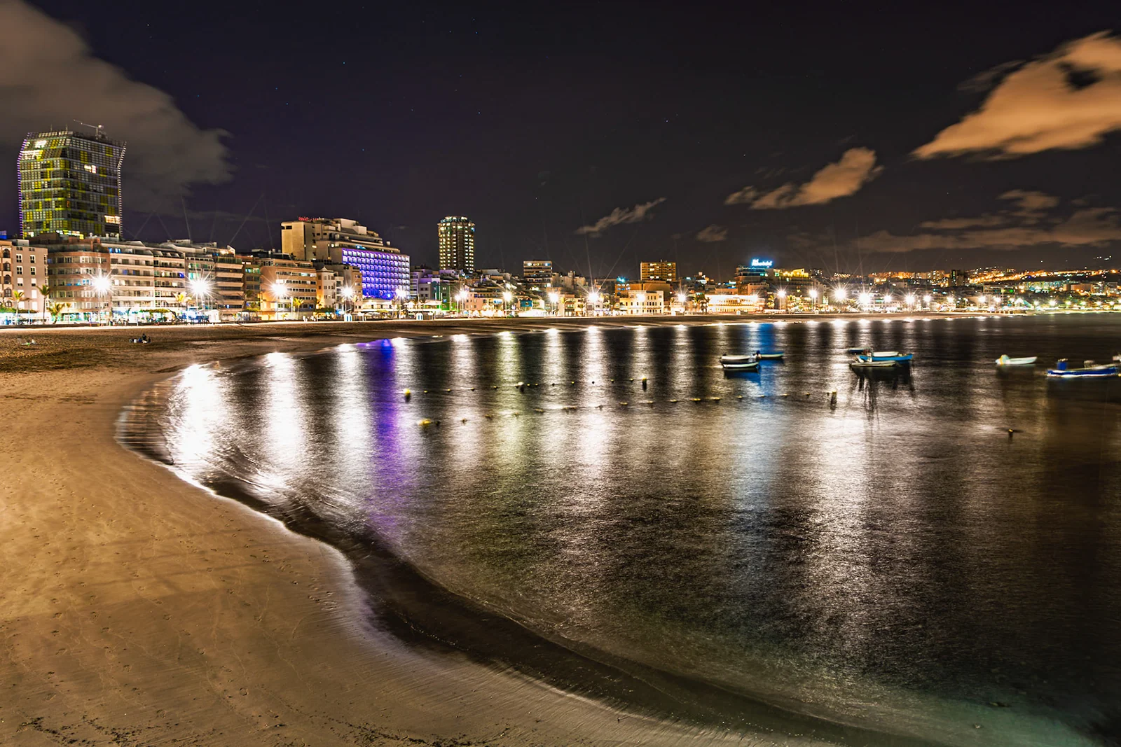 City lights reflected across a curved urban beach at night.