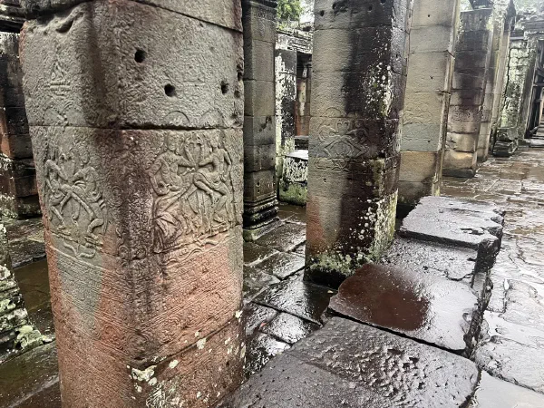 Weathered relief carvings on columns above a wet stone floor.