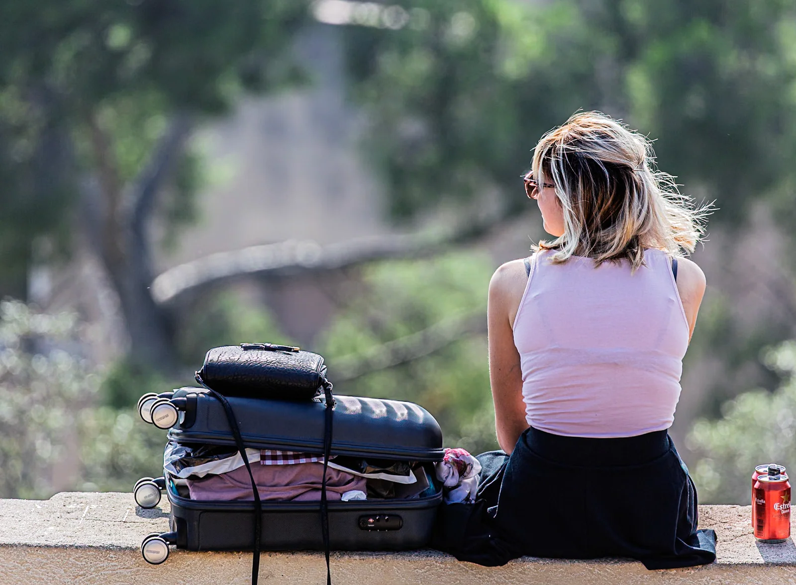 A traveller sitting beside luggage under leafy trees.