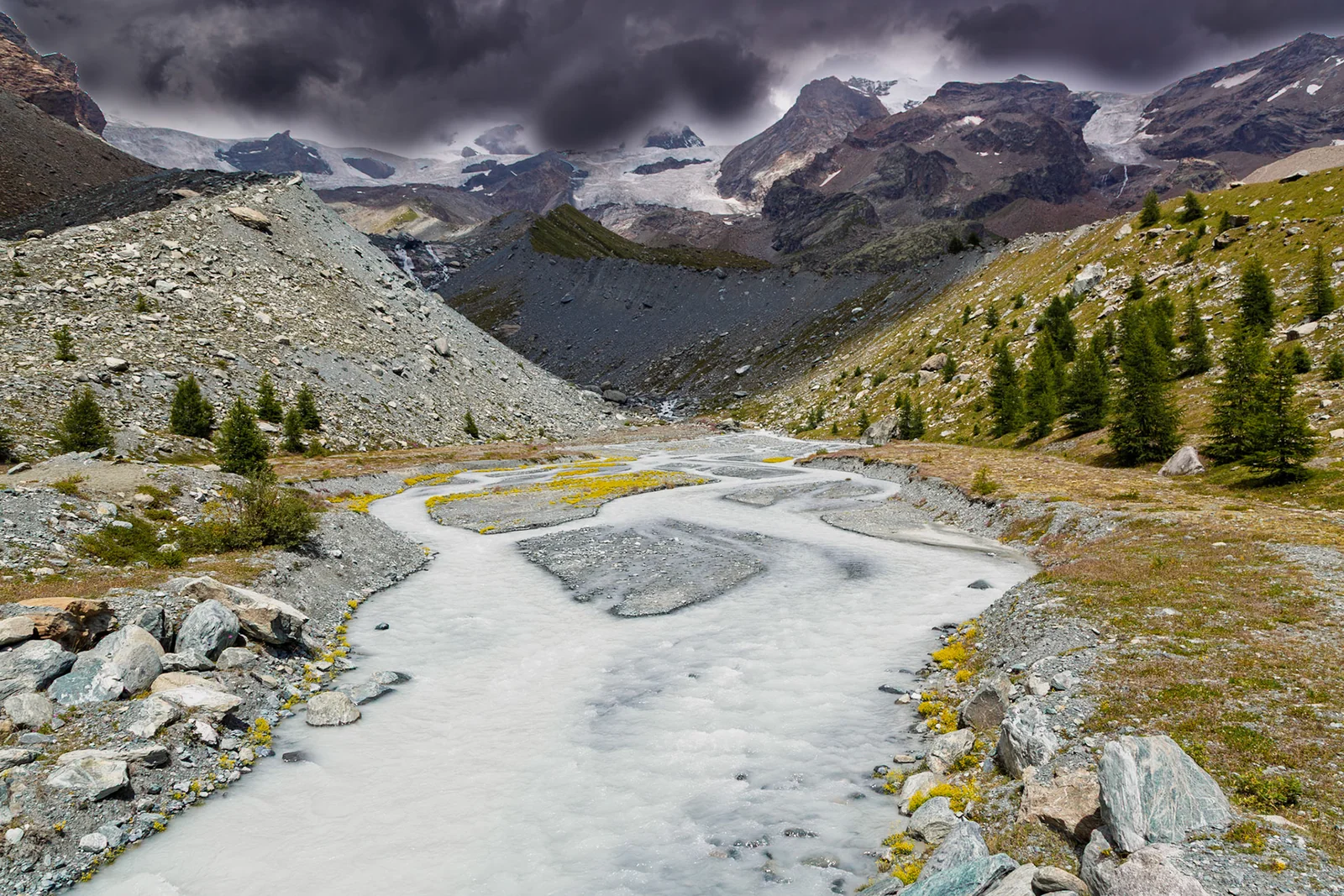 A pale mountain stream winding through a rocky valley.
