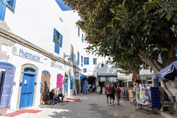 A shaded street lined with white walls, blue doors and small shops.