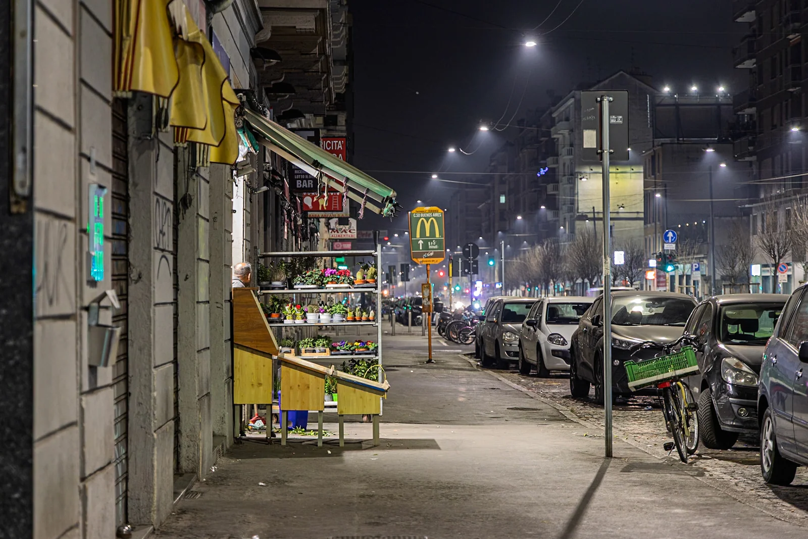 A person walking along a city pavement under streetlights.