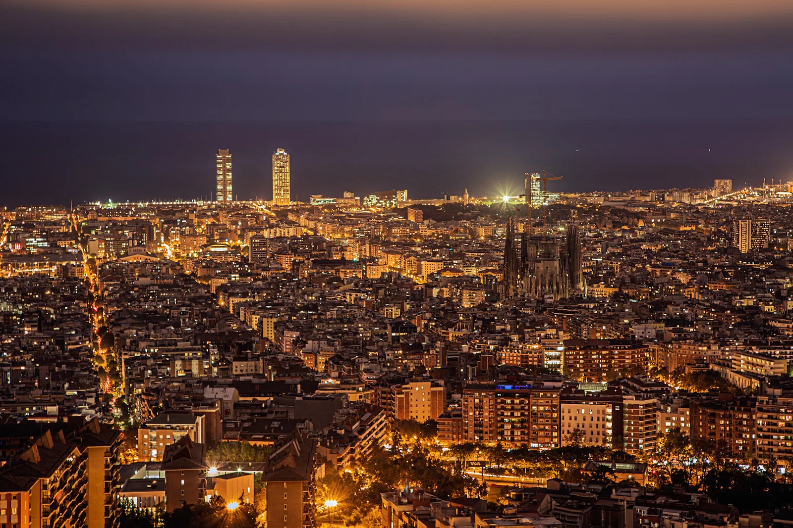 A dense city seen from above at dusk, with twin towers on the horizon.