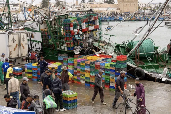 Workers and stacks of colourful crates beside fishing boats.