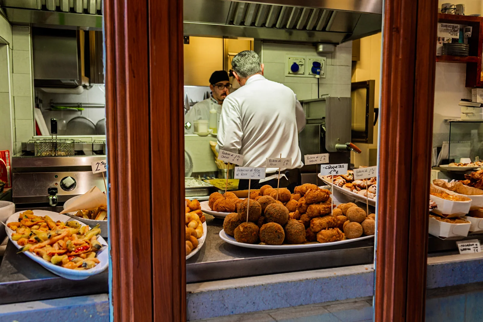 A cook working behind a counter filled with fried food.