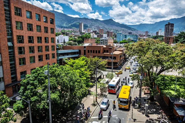 A city street with yellow taxis, red brick buildings and green hills behind them.