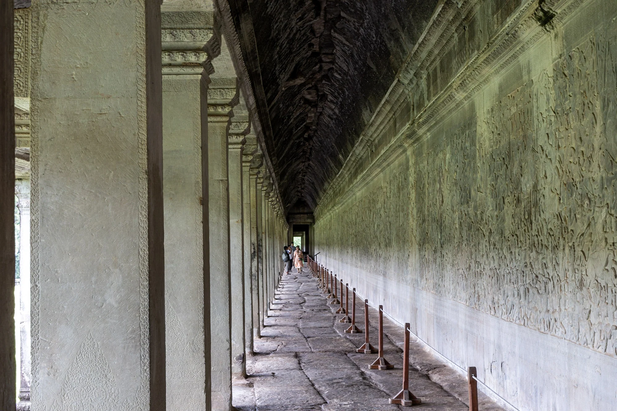 A long stone colonnade beside a wall of carved reliefs.