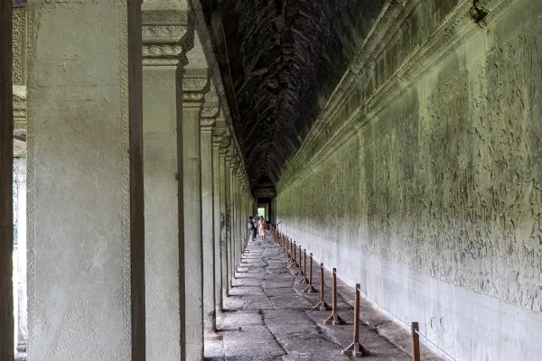 A long stone colonnade beside a wall of carved reliefs.