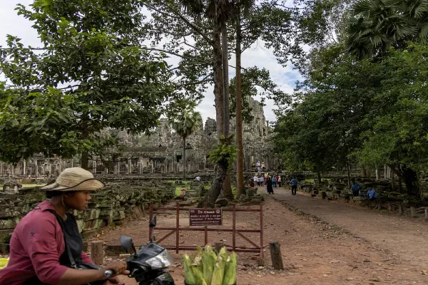 A vendor with a motorbike beside a tree-lined temple approach.