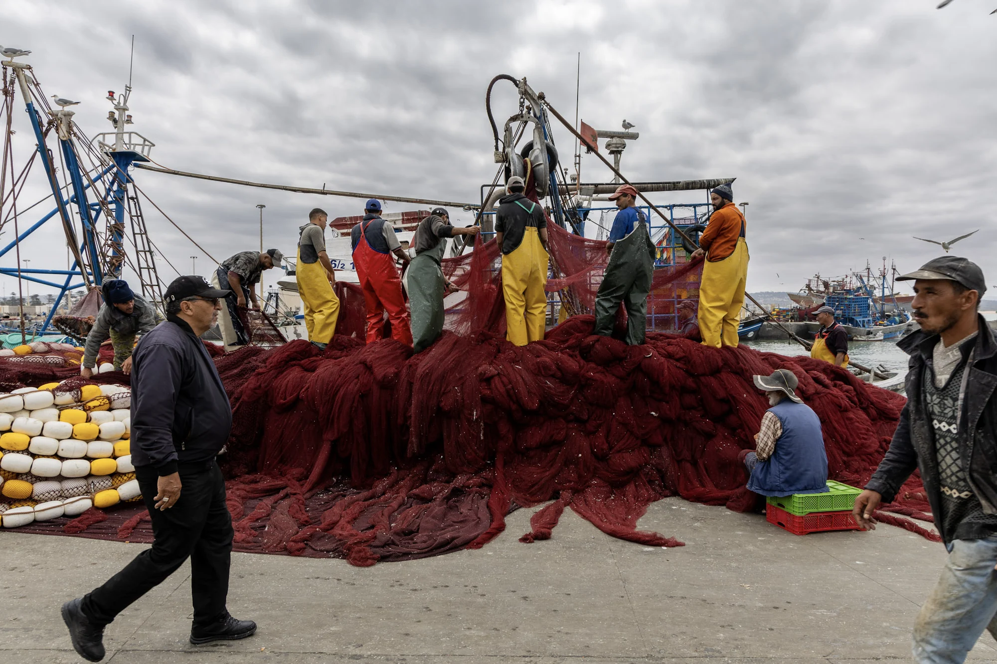 Fishermen working together on a large red net in the harbour.
